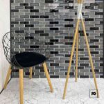 Malla decorativa de vidrio hamilton 30 x 32 3 cm-tiles-2-ok | Plomería García Modern interior corner with a black wire chair and a tall wooden tripod lamp against a gray glass-tile wall and white tiled floor.